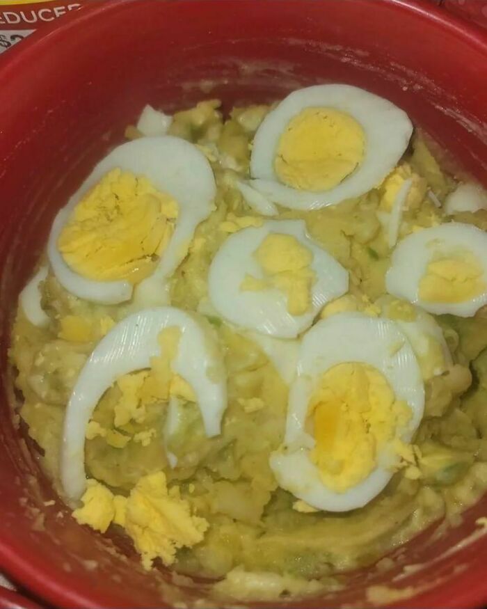 Unappetizing food with sliced boiled eggs on mushy mixture in a red bowl.