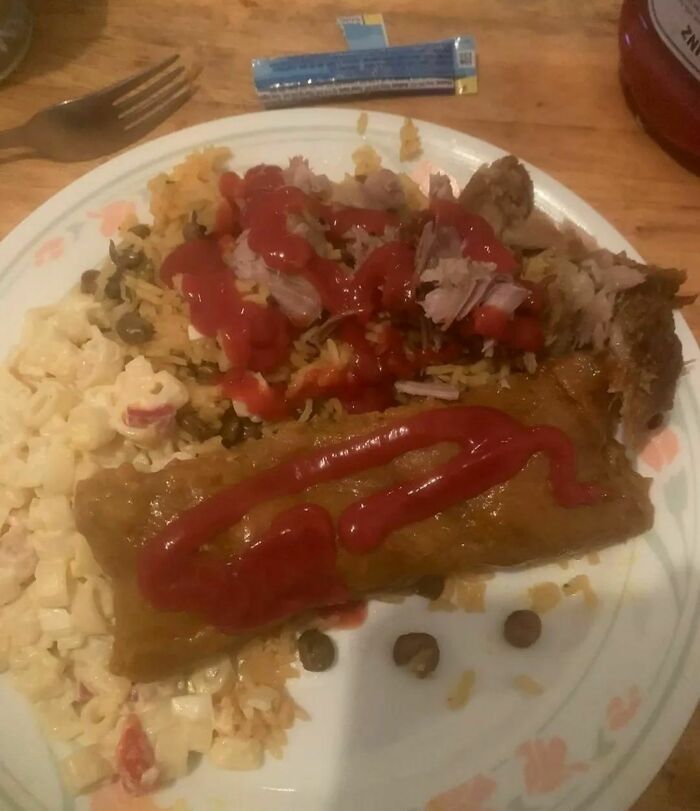 Unappetizing food on a plate with ketchup over mixed dishes, including meat and pasta.