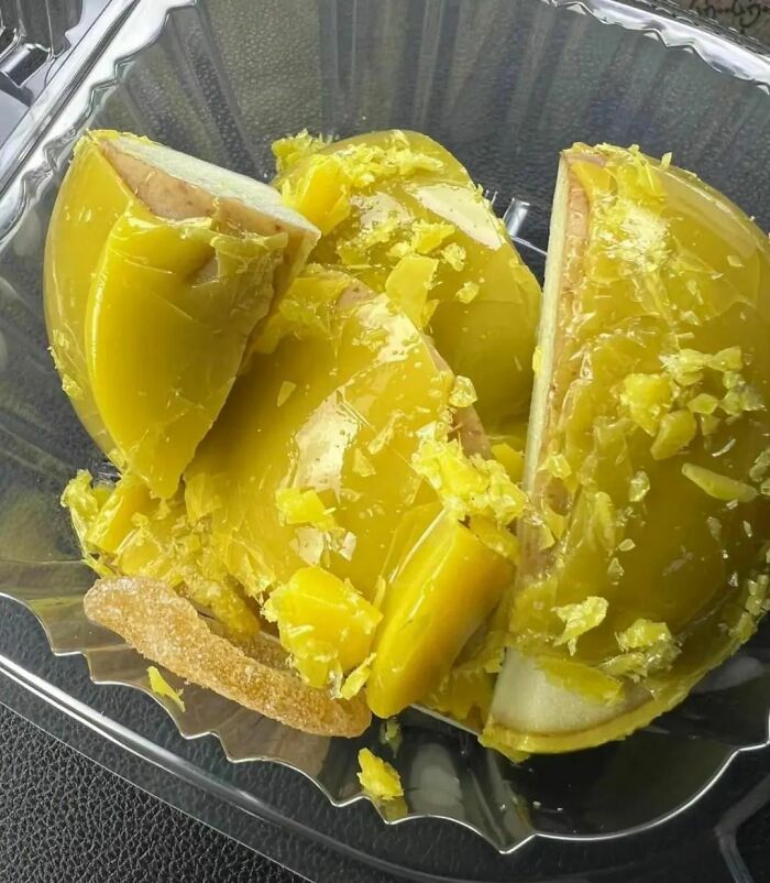 Unappetizing food photo with sliced green apple coated in an uneven yellow substance in a plastic container.
