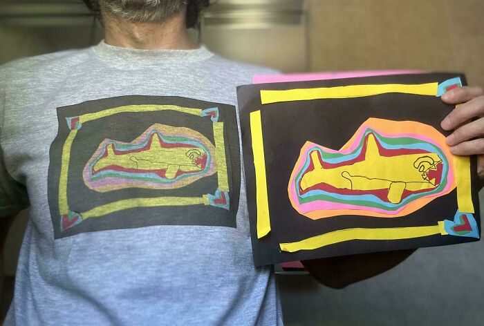 Man wearing a gray shirt with a colorful shark drawing matching the handmade shark artwork he is holding, showcasing funny dad moments.