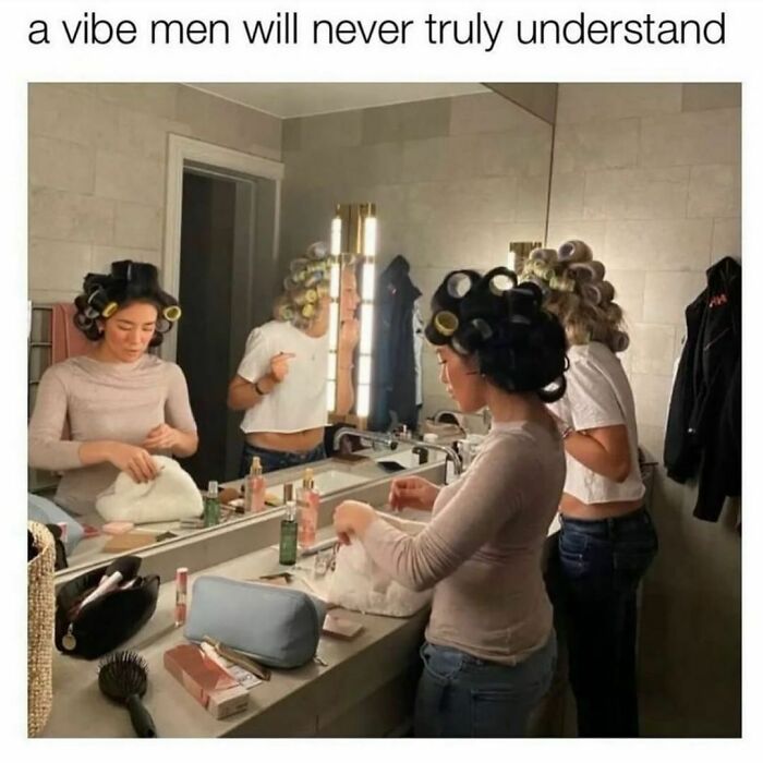 Women with hair rollers getting ready in a bathroom, surrounded by makeup and beauty products, capturing a relatable meme moment.