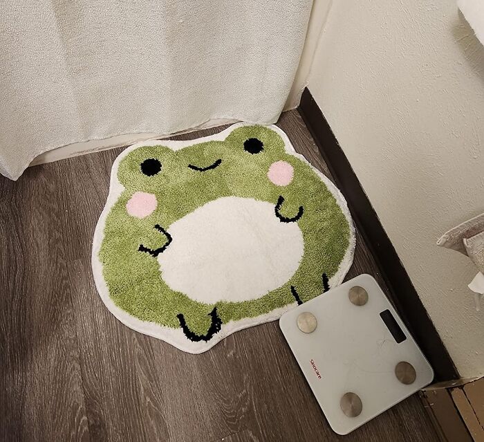Bathroom products: Frog-themed bath mat on the floor beside a digital scale, enhancing decor and functionality.