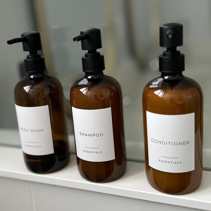Three amber bottles labeled body wash, shampoo, and conditioner on a bathroom shelf.