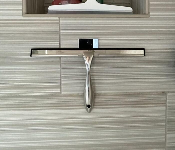 Modern bathroom squeegee with stainless steel handle on a tiled shower wall.