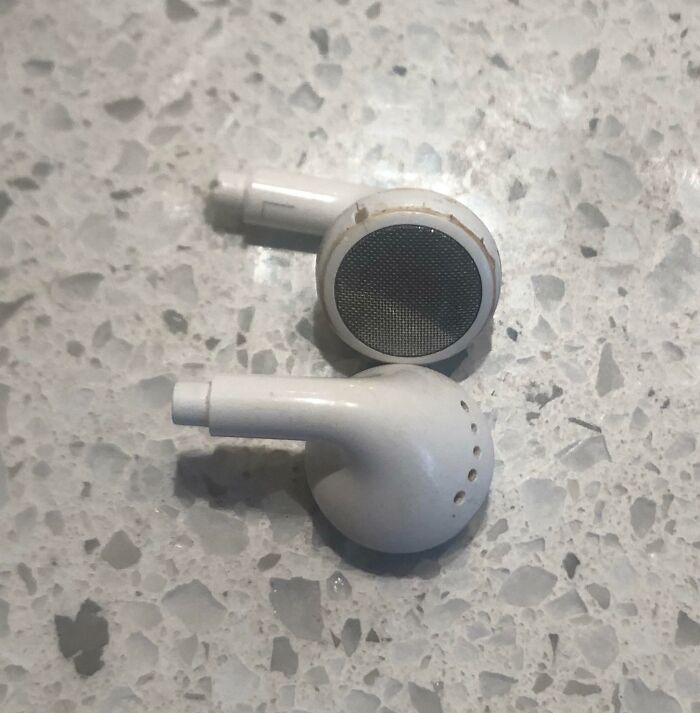 Worn and dirty wireless earbuds on a textured surface, illustrating a relatable moment for parents having a pretty miserable day.