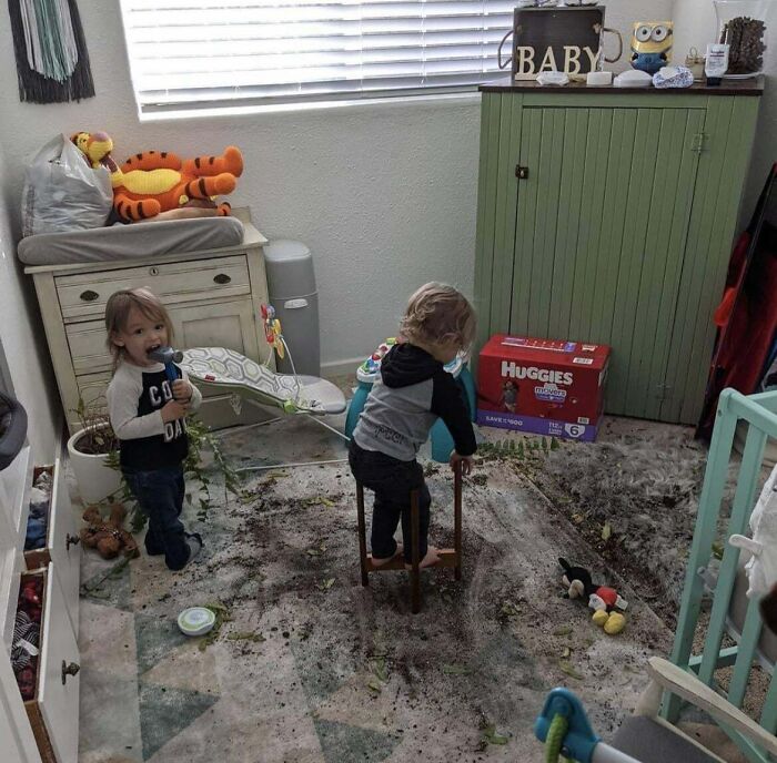 Two toddlers making a mess with dirt inside a nursery, capturing a typical parents' pretty miserable day moment.