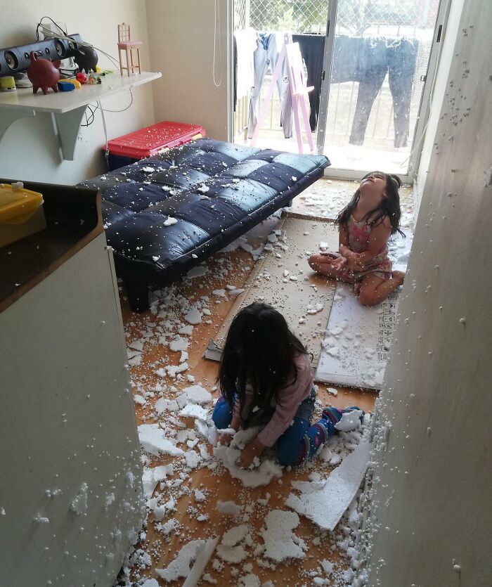 Two children sitting on the floor surrounded by broken white foam pieces, creating a messy scene for parents to clean up.