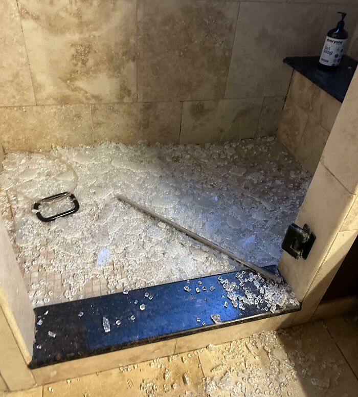 Broken glass scattered all over a shower floor and bathroom tiles showing parents having a pretty miserable day.