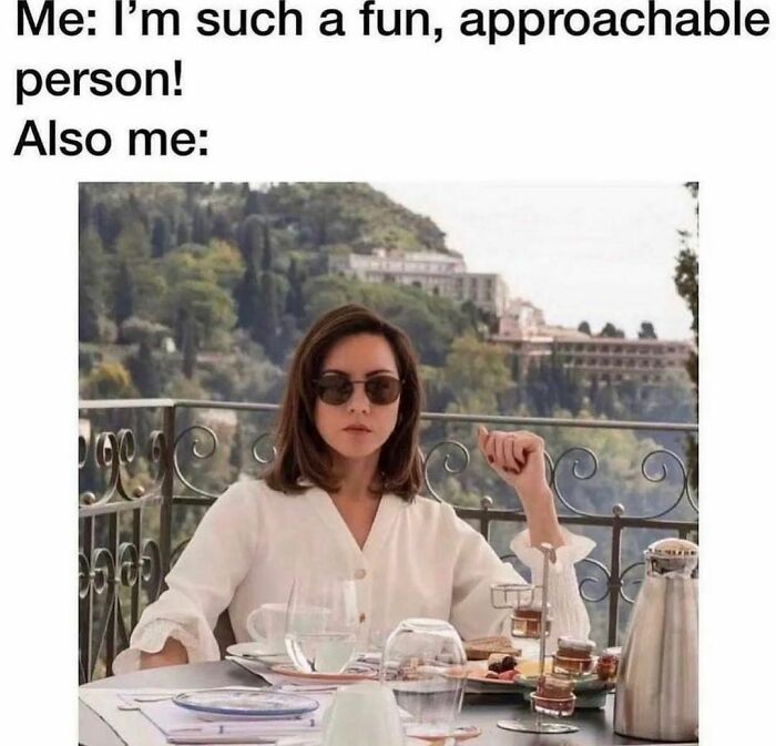 Person sitting at an outdoor café table, wearing sunglasses, looking serious; relates to barely functioning memes.