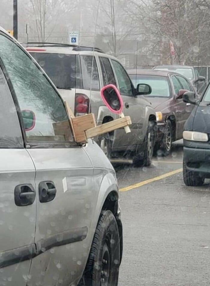 Car in parking lot with a makeshift side mirror made from wood and a pink handheld mirror, showcasing random memes humor.