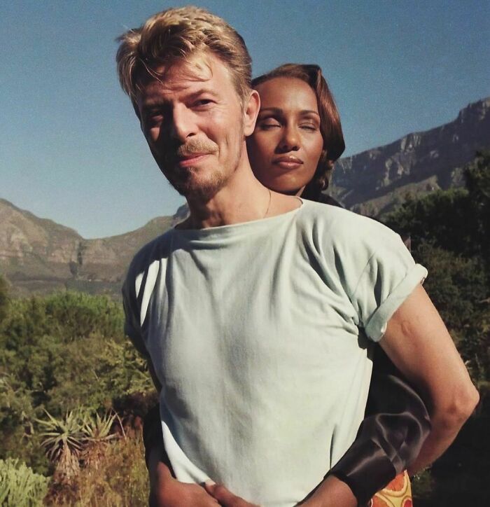 A couple embracing outdoors with mountains in the background, capturing a moment of nineties nostalgia.