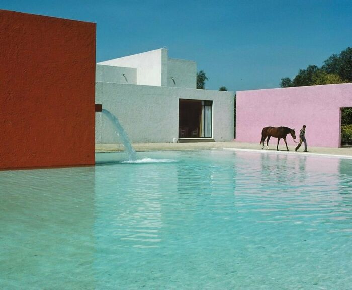 Modern 90s architecture with colorful walls by a pool, featuring a person walking a horse under a clear blue sky.