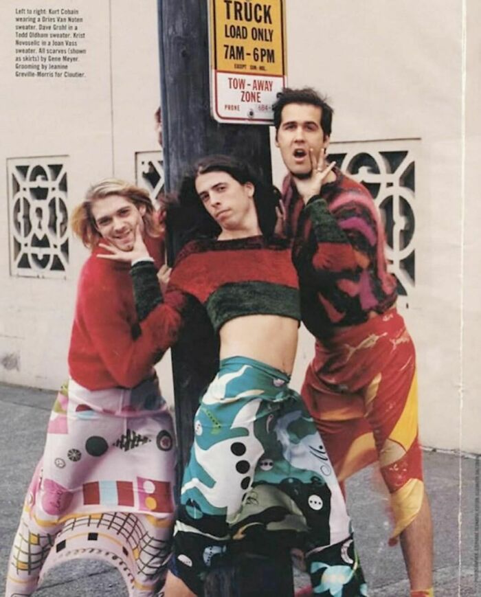 Three people in bold, colorful '90s outfits posing playfully near a street sign, embodying Nineties style and nostalgia.