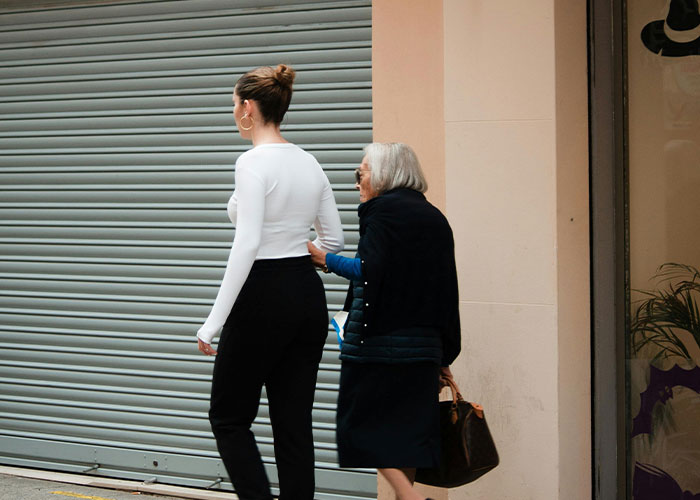 Young woman and elderly lady walking together on street, illustrating strange childhood realities people later questioned.