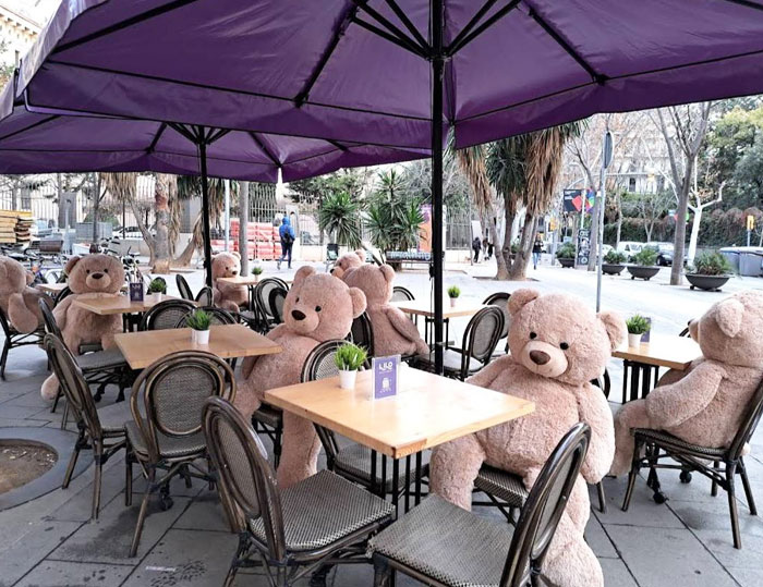 Outdoor bar seating with large teddy bears at tables under purple umbrellas, showcasing creative bars and restaurants.