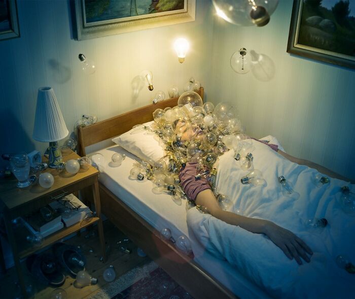 A surreal photo manipulation featuring a person in bed surrounded by glowing light bulbs.