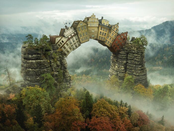 Surreal photo manipulation by Swedish Photoshop master, featuring buildings forming a bridge between rock pillars.