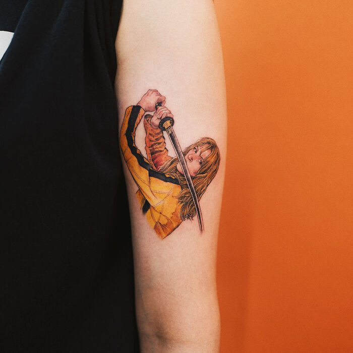 Realistic tattoo of a woman with a sword on an arm against an orange background.