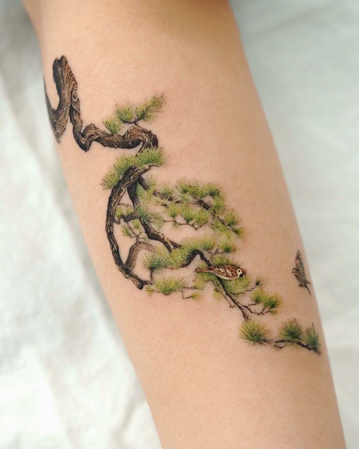 Realistic tattoo of a tree branch with green leaves and a small bird on skin.
