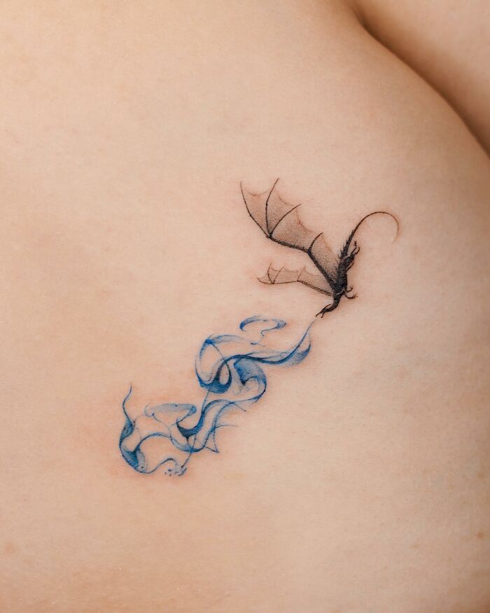Realistic dragon tattoo with blue smoke on skin.