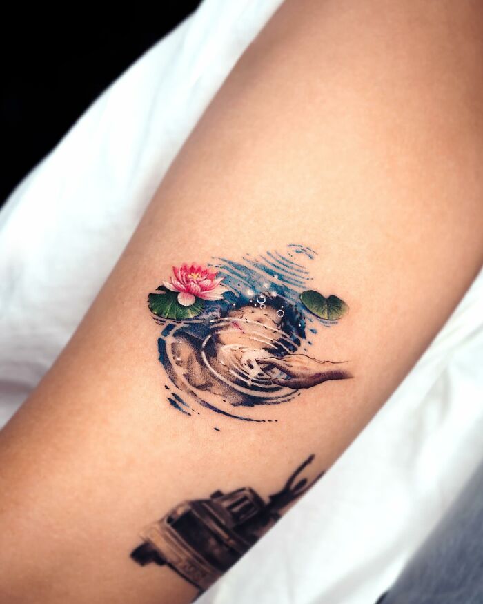 Realistic tattoo of a hand touching water with a lily pad and flower on skin.