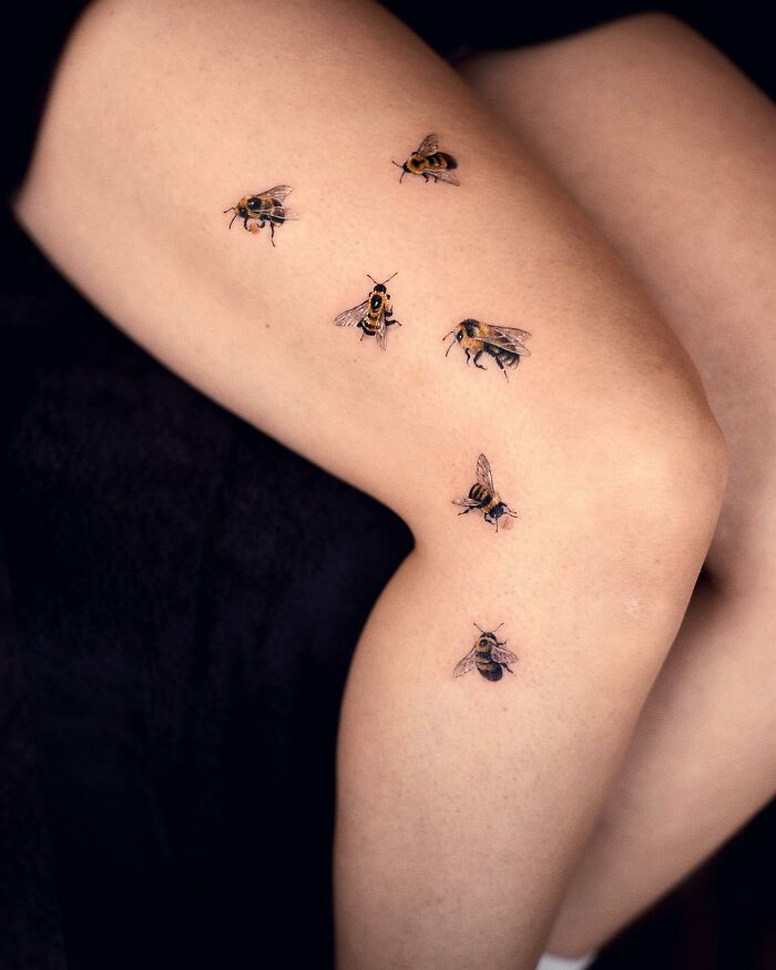 Realistic tattoos of small bees on a person's leg, showcasing the artist's detailed work.