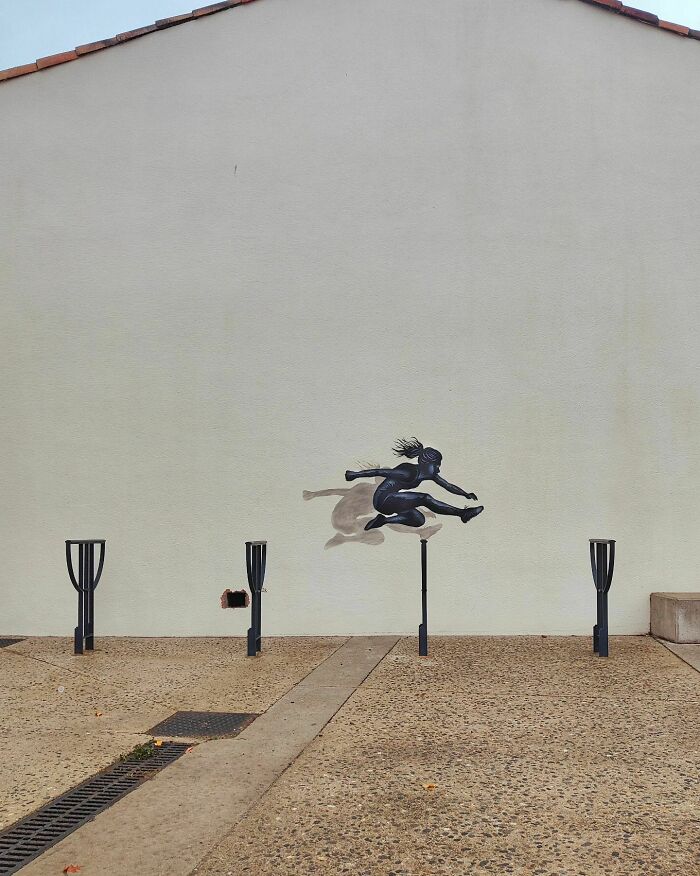 Street art featuring a painted figure leaping over pole-like structures, creatively integrated into the urban landscape.