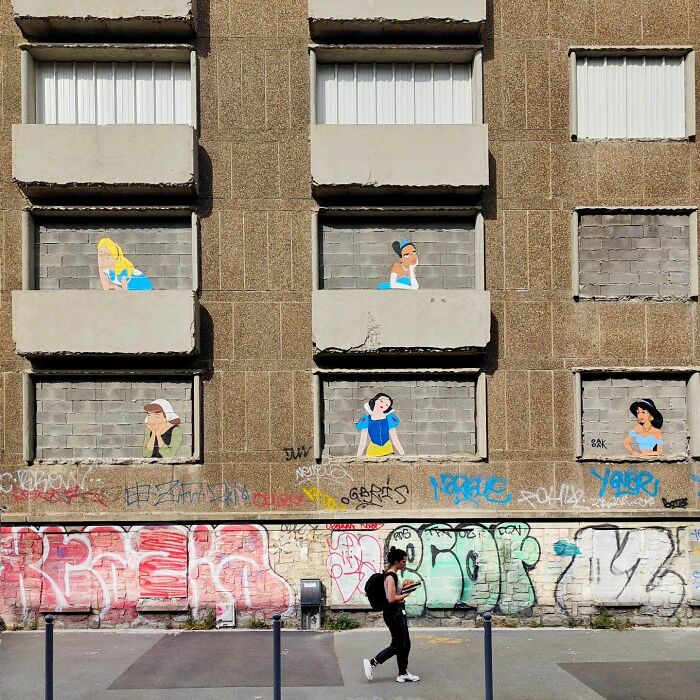 Humorous street art by Oakoak featuring cartoon characters on a building, with a person walking by.