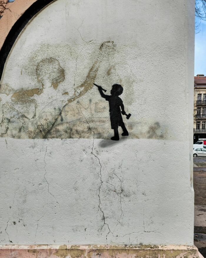 Silhouette of a child painting on a wall, creating humorous street art by Oakoak.