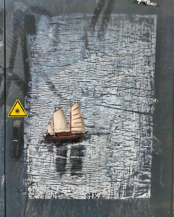 Sailing boat incorporated into street art by Oakoak, blending humorously with the textured urban backdrop.