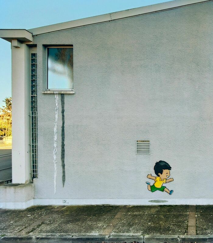 Street art of a boy jumping on a building wall by Oakoak, humorously interacting with surroundings.