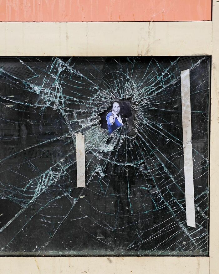 Humorous street art by Oakoak featuring a creative use of a shattered window with a pointing figure.