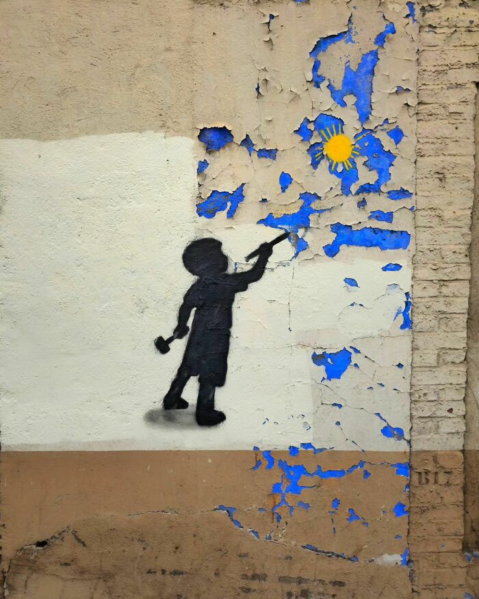 Silhouette of a child painting a sun, humorous street art piece by Oakoak integrated into peeling wall.