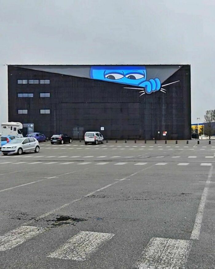 A humorous street art piece by Oakoak shows a blue character peeking from a building corner.