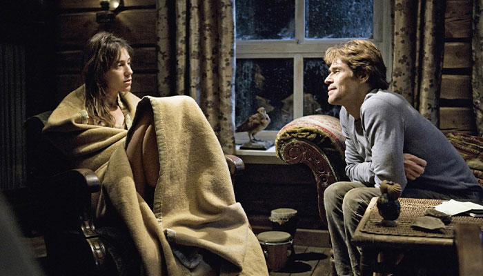 Two movie stars wrapped in a blanket, sitting across from each other in a cozy room, sharing an intense moment.