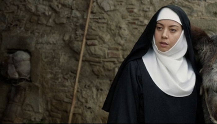 Woman in a nun outfit in a stone-walled setting from a movie scene.