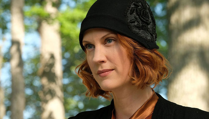 Woman with red hair in a black hat, gazing thoughtfully.