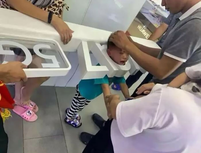 Child stuck in a play structure while parents try to free him, capturing a moment of parents having a pretty miserable day.