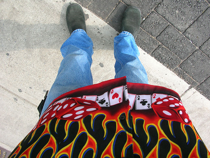 Person wearing low-rise jeans showing a whale tail under colorful flame-patterned shirt with dice and playing card designs.
