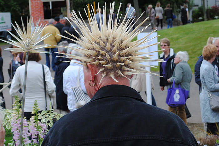 Person with spiked hair resembling a whale tail among a crowd at an outdoor event, showcasing a bold fashion trend.