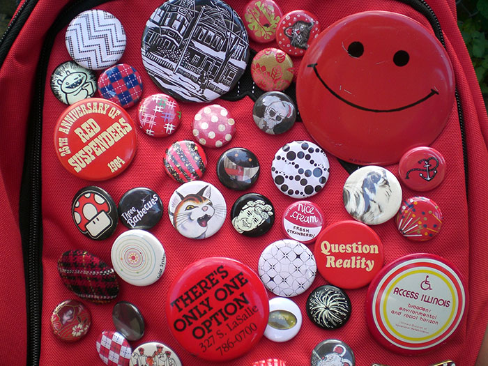Red backpack covered with various colorful pins and buttons, illustrating millennial trends including farmhouse and pop culture icons.