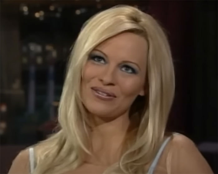 Woman with long blonde hair and blue eyeshadow smiling during a nighttime interview about whale tail trend.