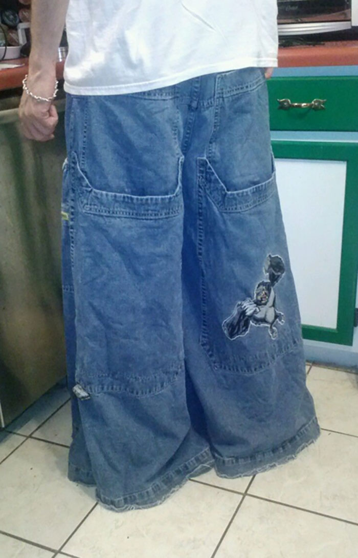 Person wearing oversized denim pants with superhero patch, a nostalgic millennial trend related to whale tail fashion cringe.
