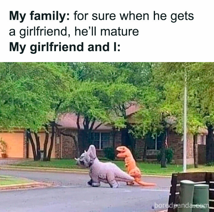 Two people in dinosaur costumes walk down a suburban street, illustrating family humor.