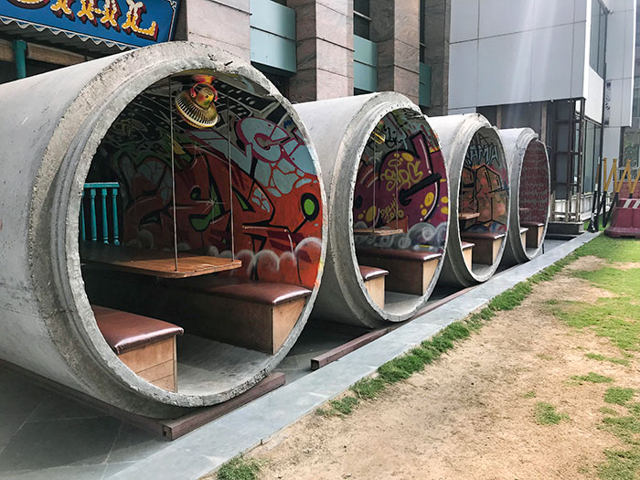 Innovative bars and restaurants featuring concrete pipe seating with colorful graffiti art inside urban outdoor setting.
