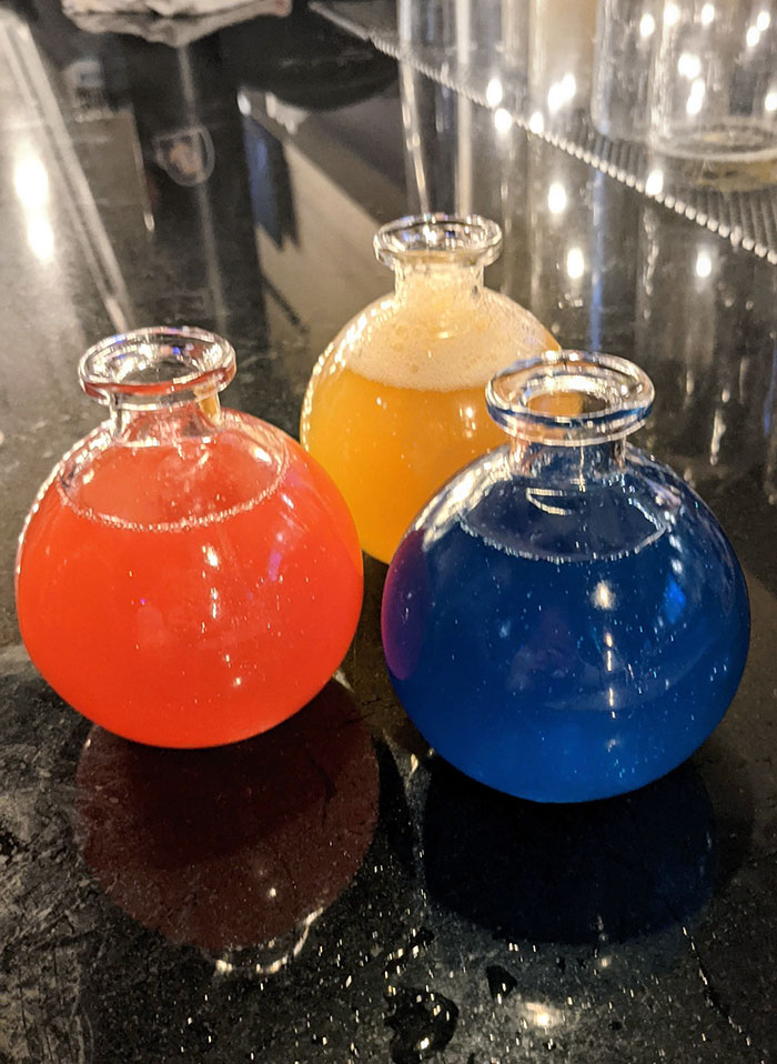 Colorful drinks served in round glass bottles on a reflective bar countertop in a creative bar setting