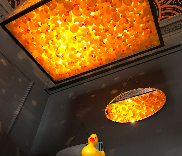 Creative bar interior with bright yellow rubber duck decorations illuminating the ceiling and mirror reflections.