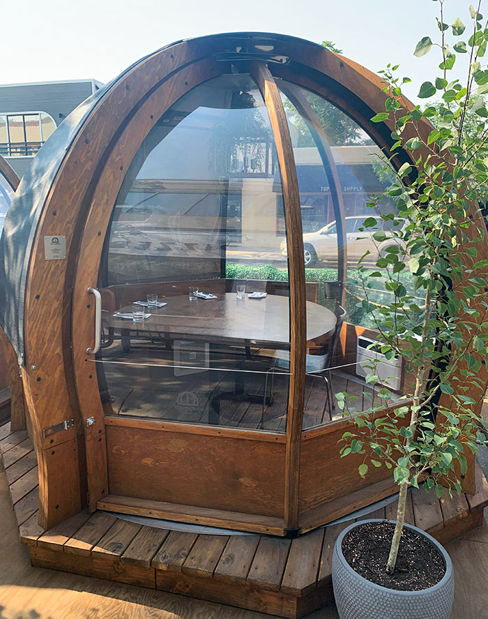 Wooden private dining pod with glass walls at a restaurant, showcasing innovative design among bars and restaurants.