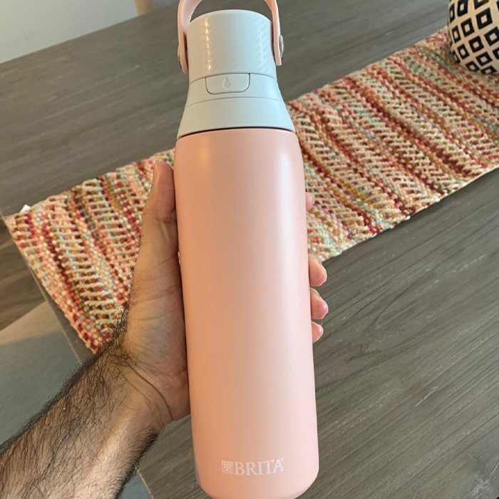 Hand holding a pink Brita water bottle, ideal for traveling light and smart on vacations.
