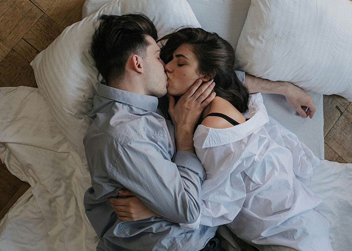 Couple embracing on a bed, both in white shirts, experiencing a close moment together.